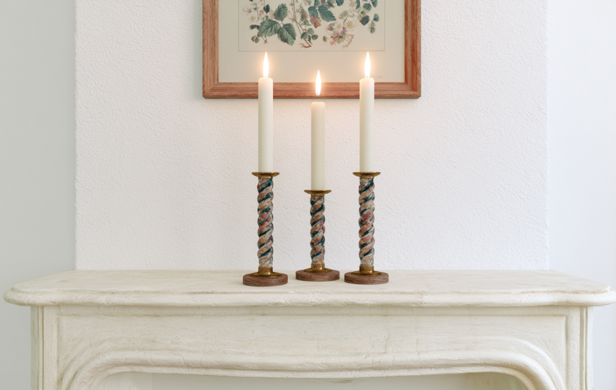 Minimalist mantel decor featuring three lit taper candles in twisted holders on a white fireplace ledge.