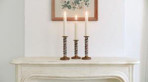 Minimalist mantel decor featuring three lit taper candles in twisted holders on a white fireplace ledge.