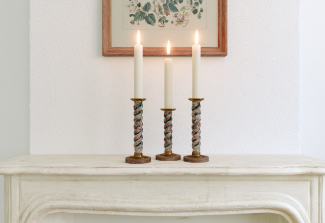 Minimalist mantel decor featuring three lit taper candles in twisted holders on a white fireplace ledge.