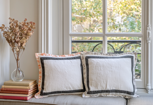 Cozy window seat decor featuring stacked books, dried botanicals in a glass vase, and tailored neutral pillows.