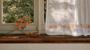 Minimalist window sill decor featuring a rustic dried branch on a wooden ledge next to a sheer curtain.