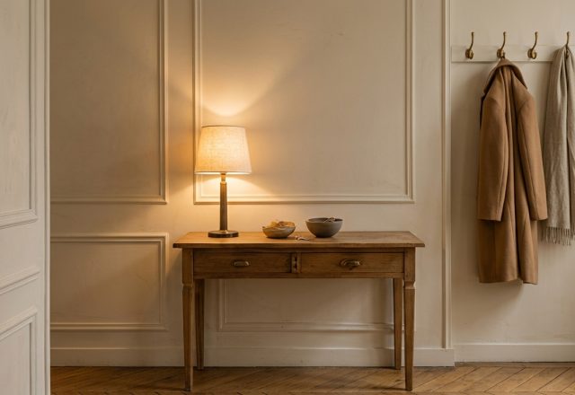 A minimalist entryway console styling featuring a vintage wooden table, a warm lamp, and wall molding.