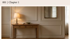 Warm entryway console styling featuring a wooden table, soft lamp glow, and traditional picture frame wall moulding.
