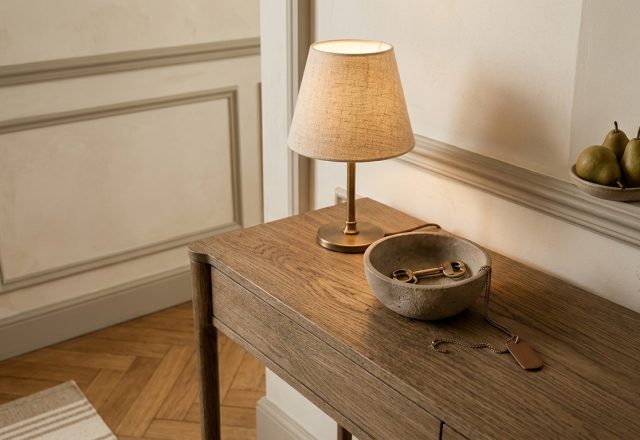 Warm entryway console styling featuring a petite linen shade lamp, stone catchall bowl, and parquet floor.