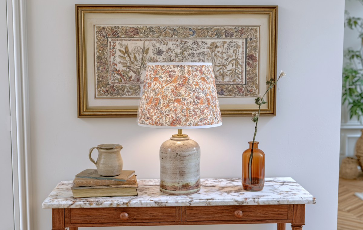 Styled entryway console table with marble top, vintage botanical art, and a patterned ceramic table lamp.