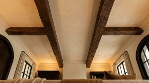 Rustic exposed ceiling beams crossing a textured plaster ceiling in a bright living space.