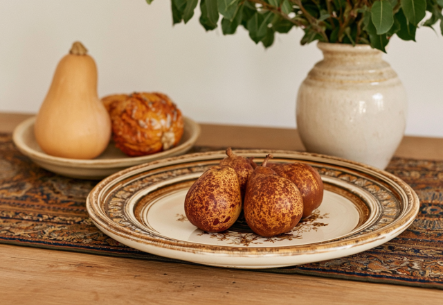 Fall tabletop styling featuring speckled pears, a ceramic vase with greens, and a squash on a wood console