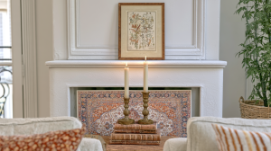 Fireplace mantel decor featuring antique brass candlesticks, vintage books, and a framed botanical illustration print.