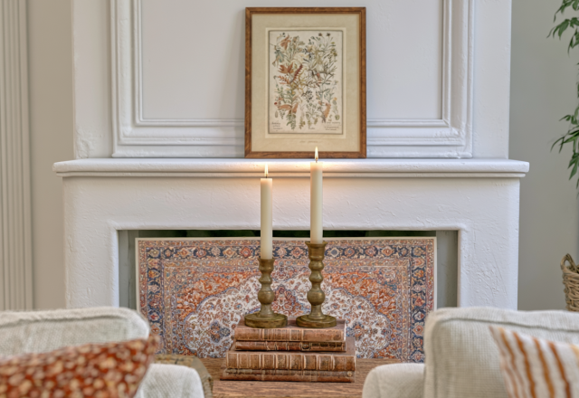 Fireplace mantel decor featuring antique brass candlesticks, vintage books, and a framed botanical illustration print.