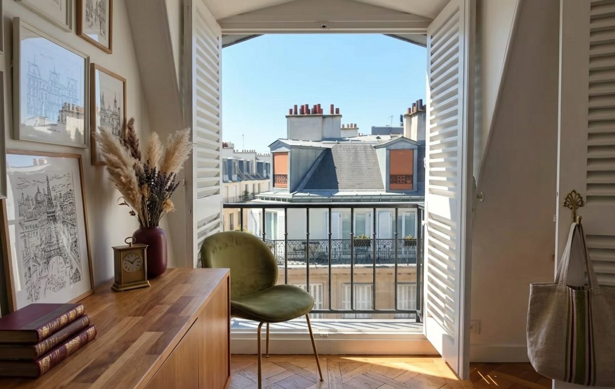 French apartment balcony with wrought iron railing and open wooden shutters overlooking Parisian rooftops