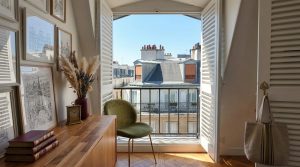 French apartment balcony with wrought iron railing and open wooden shutters overlooking Parisian rooftops