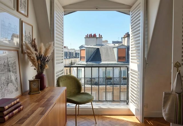 French apartment balcony with wrought iron railing and open wooden shutters overlooking Parisian rooftops