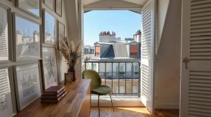 French apartment balcony decor featuring a green velvet chair and gallery wall next to open balcony doors.
