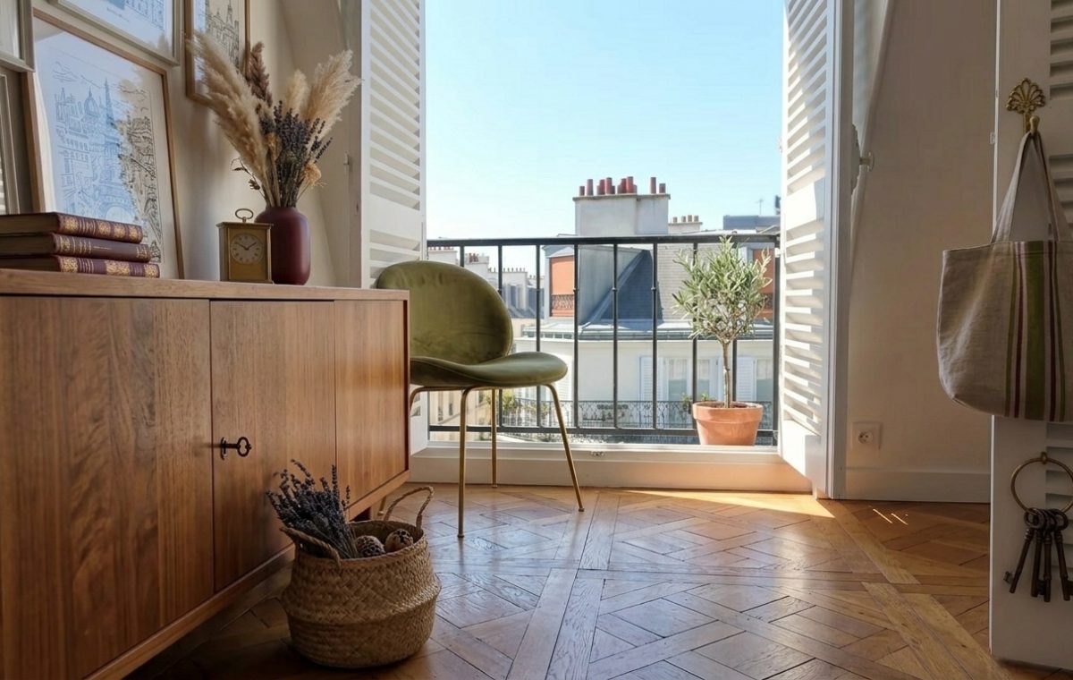Bright French apartment interior styling featuring herringbone floors, wooden sideboard, and balcony view.