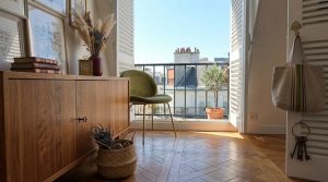 Bright French apartment interior styling featuring herringbone floors, wooden sideboard, and balcony view.