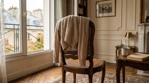 A cozy French apartment living room featuring a wooden chair with a neutral sweater and natural window light.