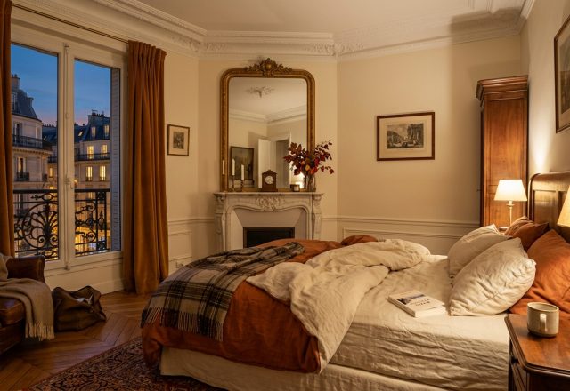 Cozy French Country bedroom featuring rust curtains, an antique fireplace, and warm evening lighting.