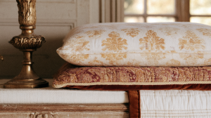 French Country bedroom styling featuring damask pillows, velvet cushions, and an antique brass candlestick on a distressed wooden surface.