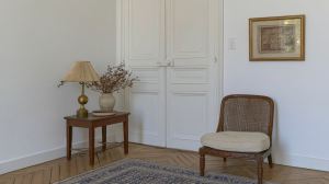 French country living room featuring a vintage side table, cane chair, and herringbone wood floors.