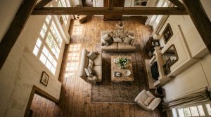 High angle view of a French Country living room featuring exposed wooden beams, neutral sofas, and rustic wood floors.