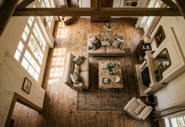 High angle view of a French Country living room featuring exposed wooden beams, neutral sofas, and rustic wood floors.