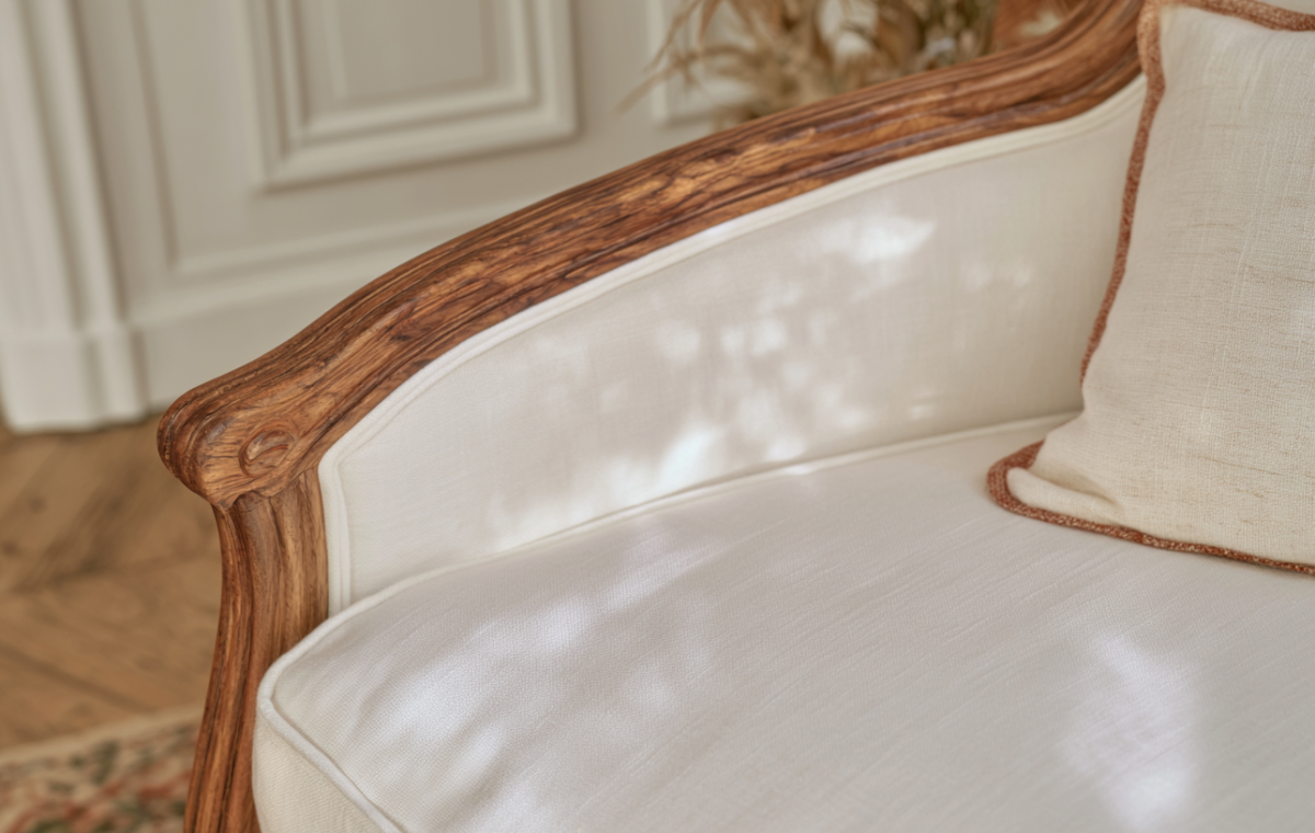 Close-up of a French country settee with carved wooden arm and cream linen upholstery.
