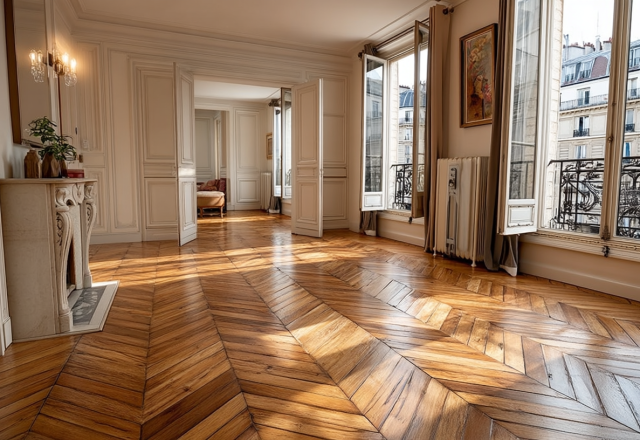 Bright historic living room featuring polished French herringbone hardwood floors and tall windows.
