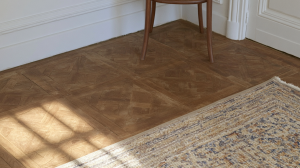 Close up of classic French parquet flooring with a textured rug and sunlight shadows.