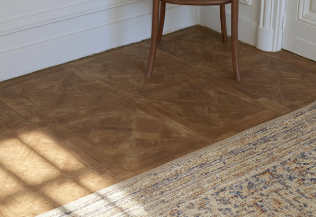 Close up of classic French parquet flooring with a textured rug and sunlight shadows.
