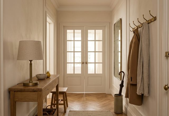 Hallway interior design with oak herringbone floors, wooden console table, and brass coat rack.
