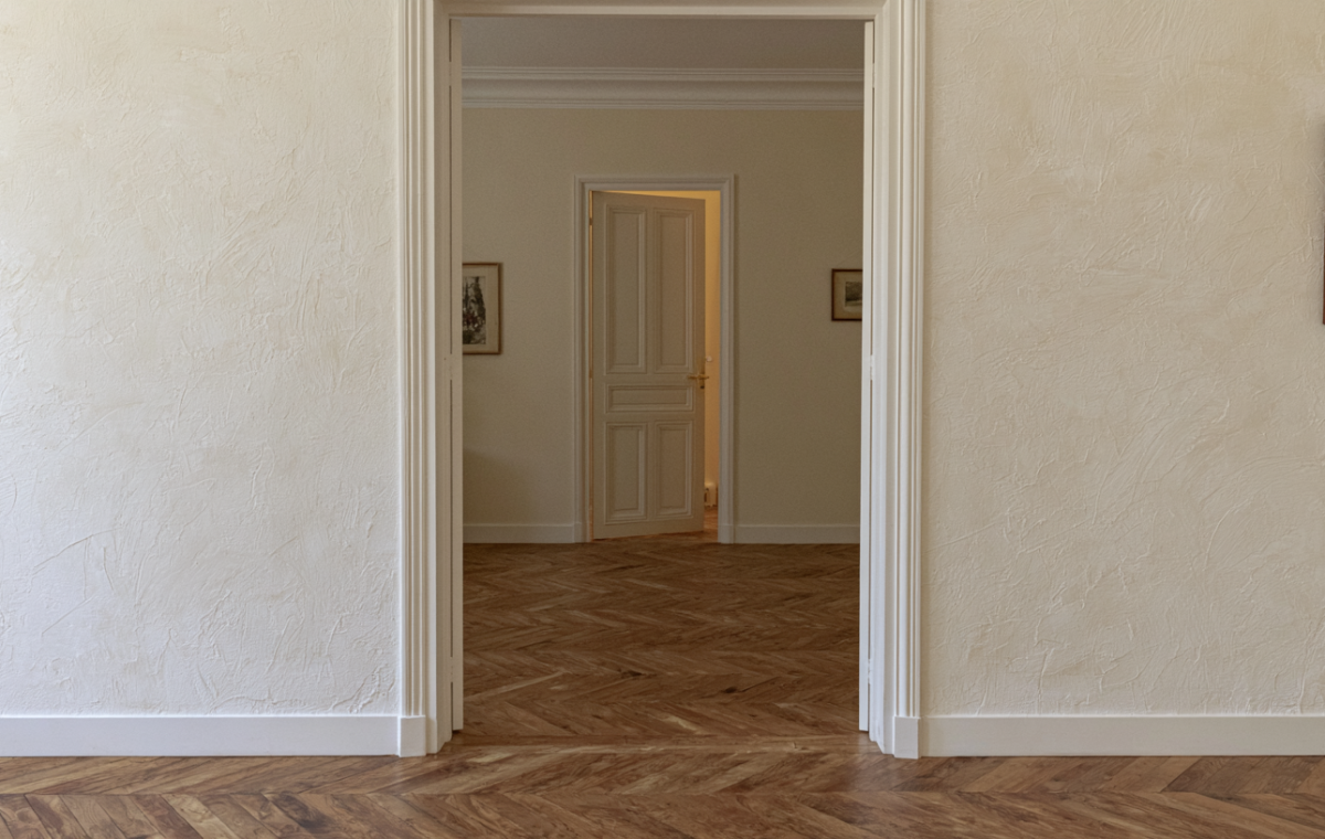 Herringbone hardwood floor transition viewed through an open interior passageway with textured neutral walls.