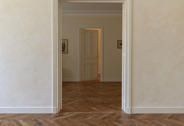 Herringbone hardwood floor transition viewed through an open interior passageway with textured neutral walls.