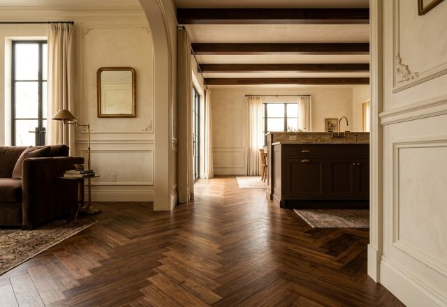 Dark herringbone hardwood floors leading through an archway into a transitional living space and kitchen.