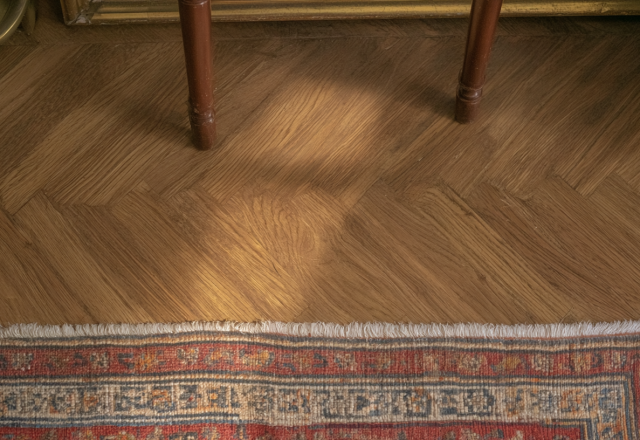 Close-up of herringbone wood flooring paired with a vintage red Persian rug and wooden furniture legs.