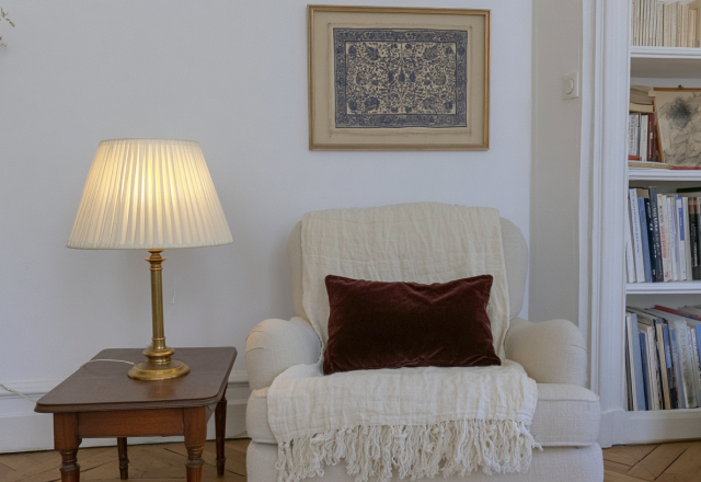 A cozy reading corner setup featuring an armchair, brass table lamp, and built-in bookshelves.