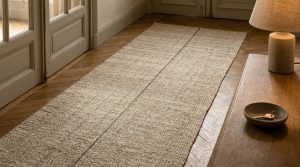 A natural fiber hallway runner rug with a central dark stripe laid over herringbone wood flooring next to a wooden console table.