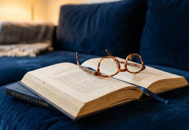 An open book with reading glasses resting on a blue velvet sofa for a cozy reading nook setup