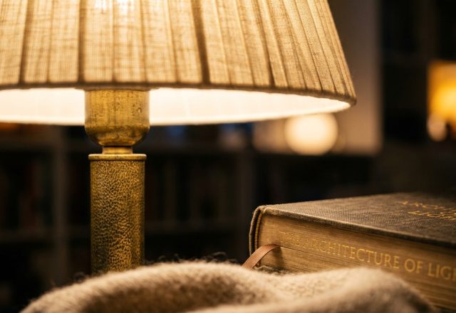 Warm reading room lighting cast by a brass lamp next to a hardcover book