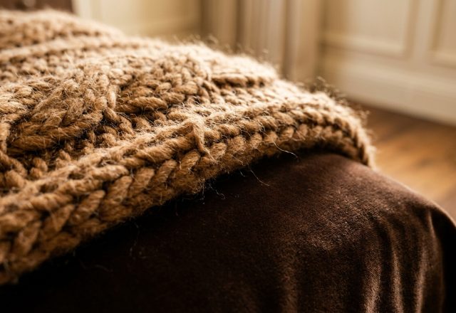 Close-up of a chunky knit blanket layered over brown velvet bedding in a cozy bedroom