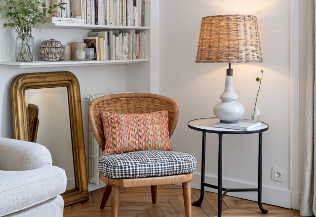Cozy corner reading nook featuring a woven accent chair, marble side table with lamp, and built-in bookshelves.