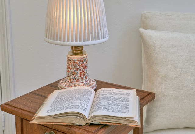 Cozy bedside reading nook featuring an open book and floral ceramic lamp on a wooden nightstand