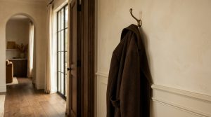 A minimalist brass hallway coat hook holding a dark coat against a neutral wall in a transitional home entrance.