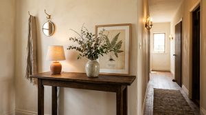 A rustic wood hallway console table styled with a lamp, vase, and botanical print.