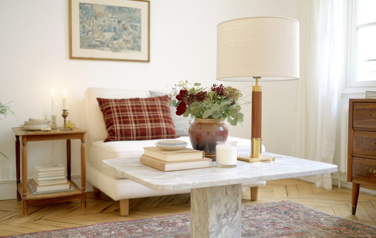 A styled marble coffee table with a brass lamp and floral vase in a neutral living room.