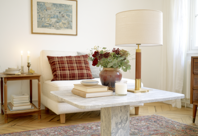 A styled marble coffee table with a brass lamp and floral vase in a neutral living room.