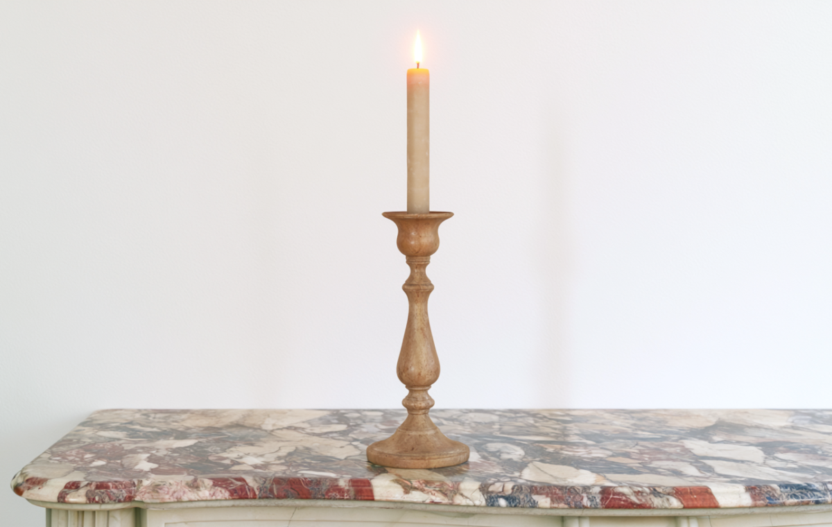 A minimalist wooden candle holder with a lit taper candle resting on an antique marble console table.