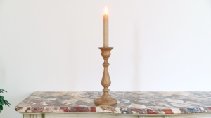 A minimalist wooden candle holder with a lit taper candle resting on an antique marble console table.