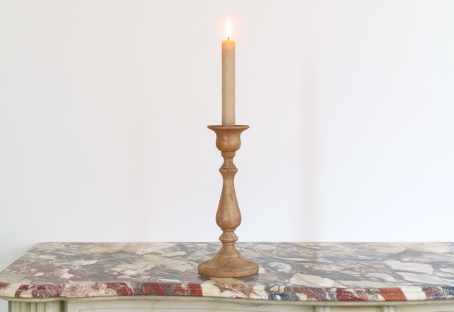 A minimalist wooden candle holder with a lit taper candle resting on an antique marble console table.