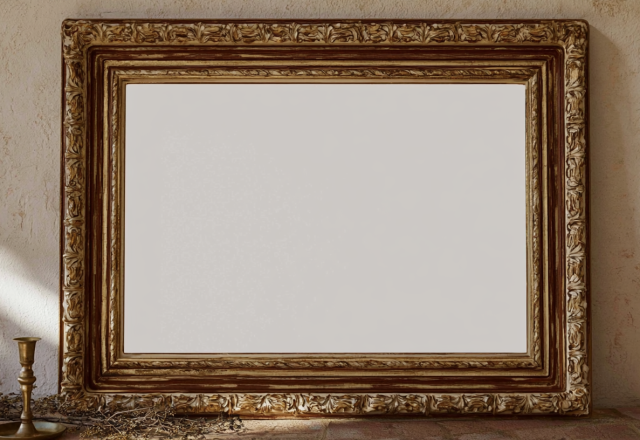 An ornate antique picture frame leaning against a textured rustic wall with a brass candleholder
