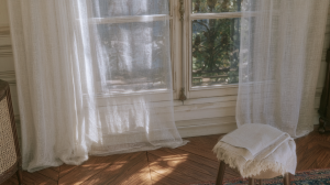 Sheer linen curtains diffusing bright natural light in a living room with herringbone wood floors and a vintage window